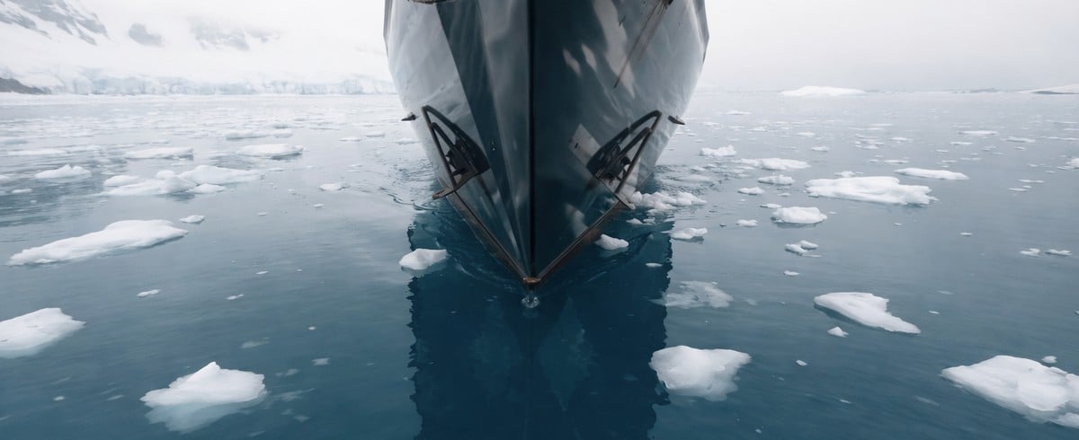 Close-up of a ship’s bow moving through cold water with scattered floating ice.